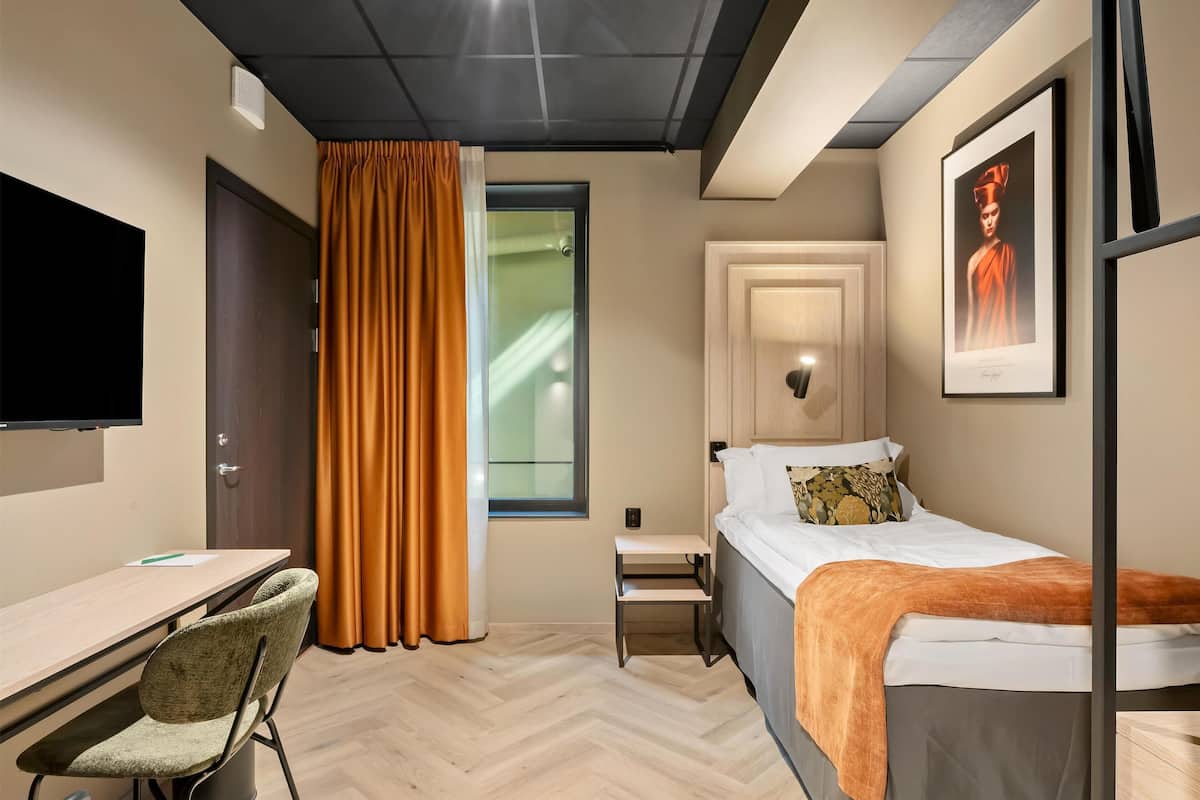 A modern hotel room with a bed, desk, chair, and a television.