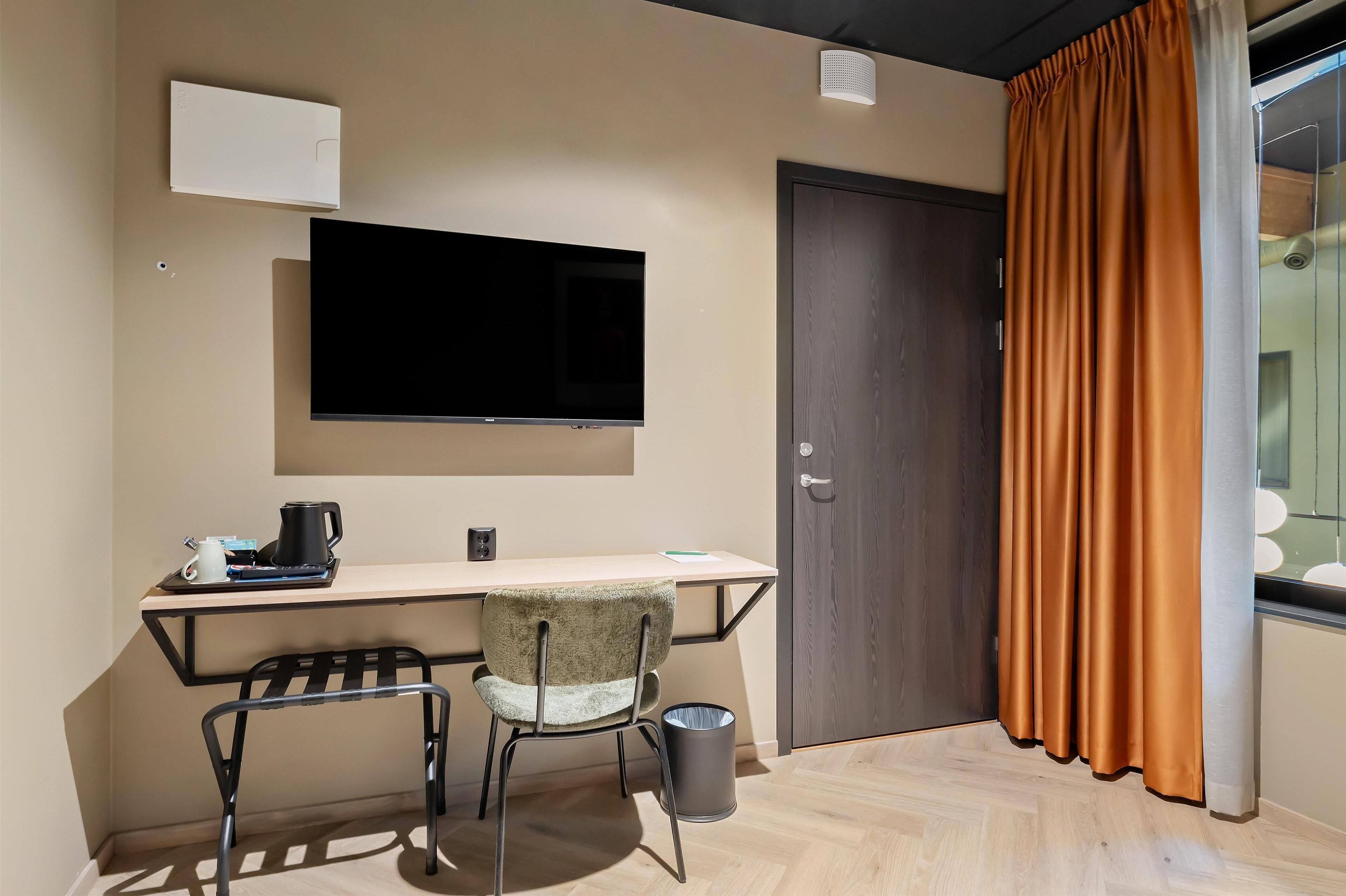 A room with a desk, chair, television, and a door with curtains.