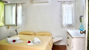 Ein Schlafzimmer mit einem Bett, einem Nachttisch, einem Spiegel, einer Klimaanlage und einem Fenster mit Vorhängen.