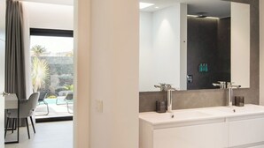 A modern bathroom with a large mirror, dual sinks, and a view of an outdoor patio with a dining area.