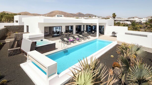 A rooftop pool area with lounge chairs, a hot tub, and a view of mountains.