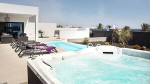 A rooftop pool area with a hot tub, lounge chairs, and a view of the ocean.