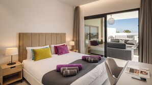 A hotel room with a bed, bedside tables, a desk, and a view of the outdoor balcony.