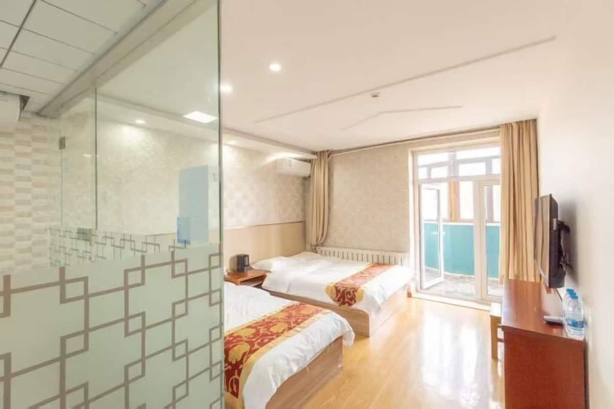 Ein Hotelzimmer mit zwei Betten, einer Glastrennwand, einem Fernseher und einem Fenster mit Vorhängen.