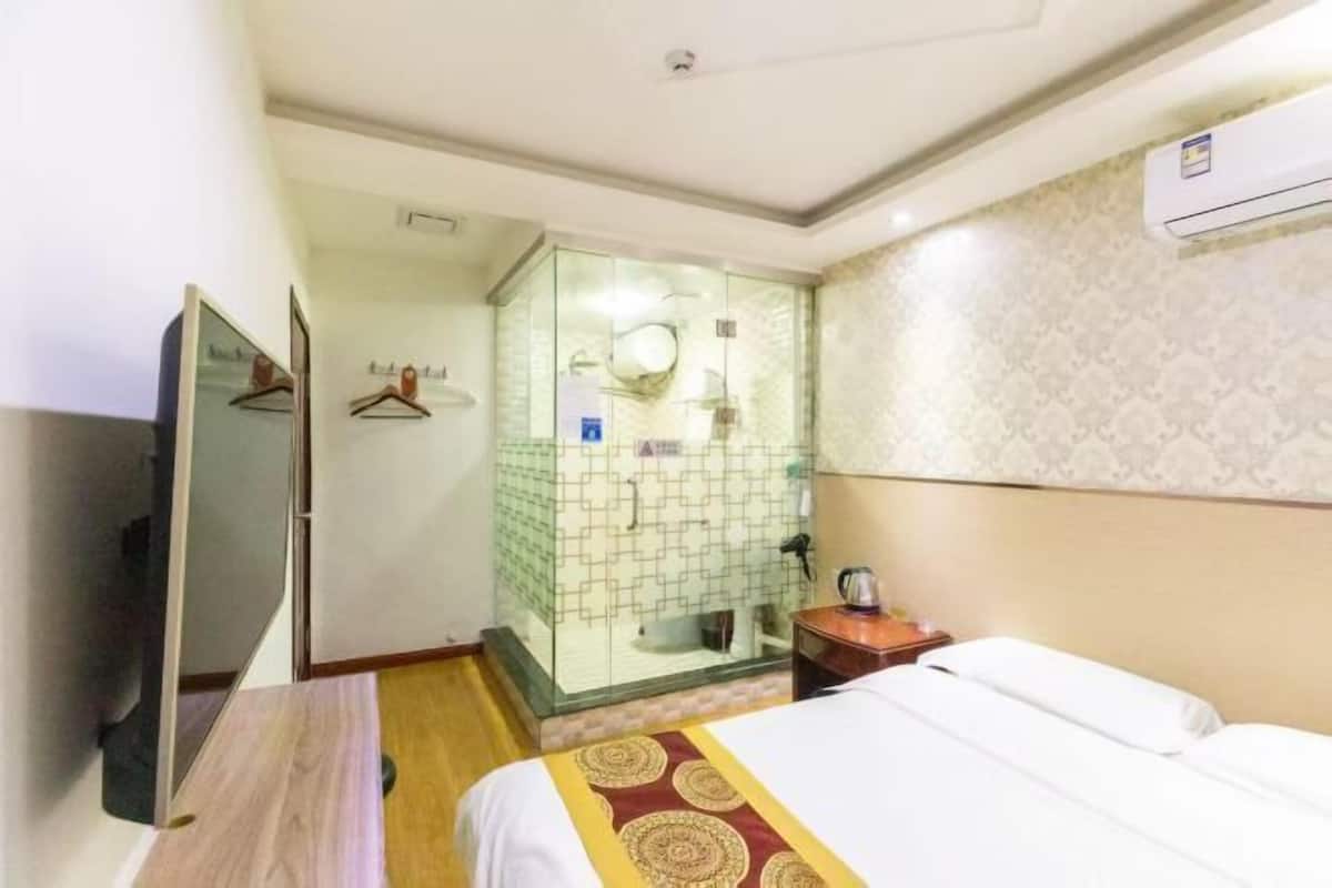 Ein Hotelzimmer mit einem Bett, einem Fernseher, einer Duschkabine und einer Wand-Klimaanlage.