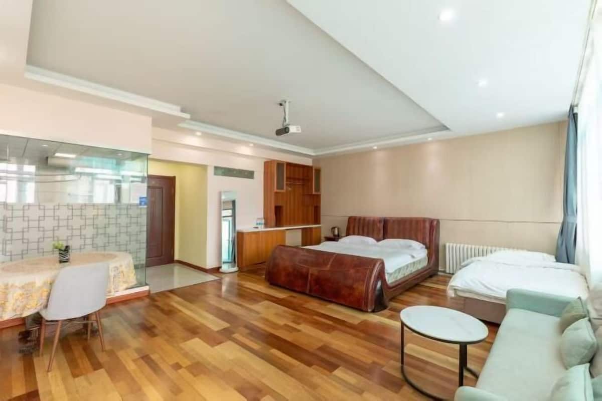 Ein modernes Hotelzimmer mit Holzboden, einem Bett, einer Couch, einem kleinen runden Tisch und einer Küchenzeile.