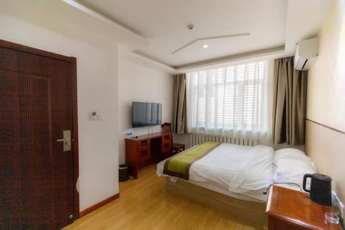 Ein Hotelzimmer mit Bett, Schreibtisch mit Stuhl, Fernseher und einem Fenster mit Vorhängen.