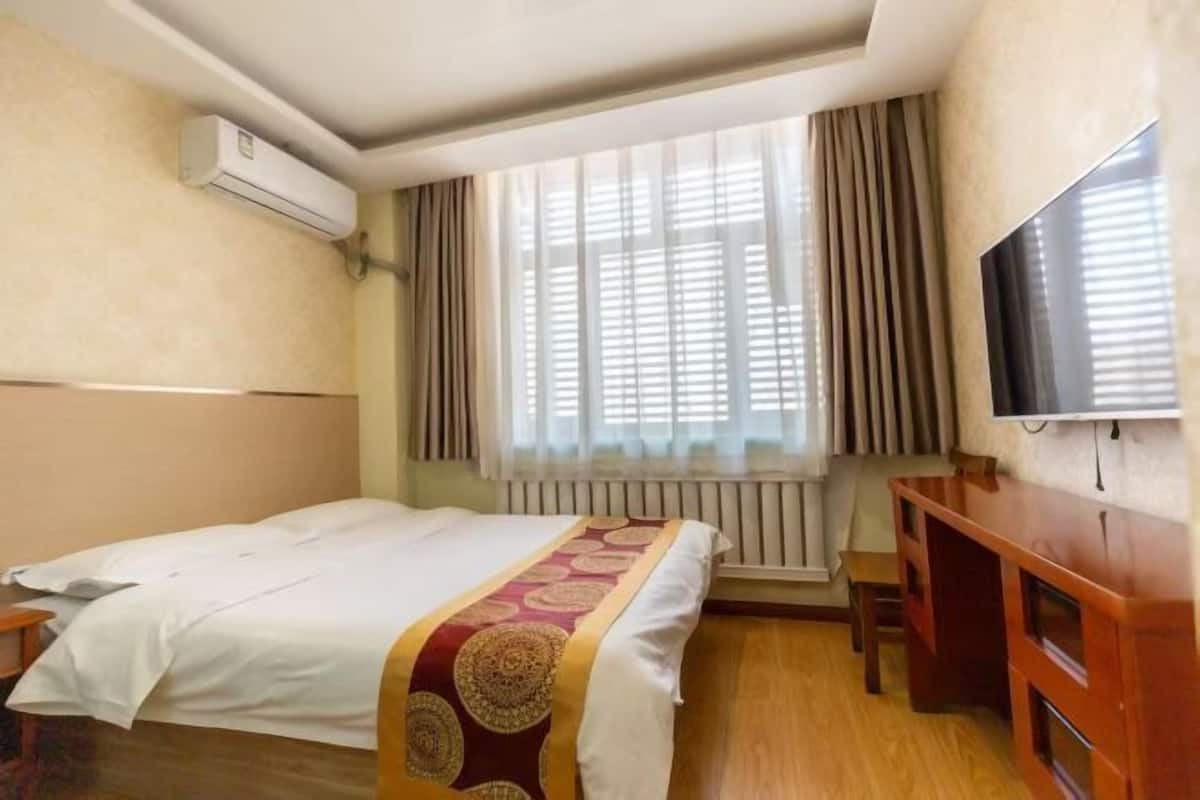 Ein Hotelzimmer mit Bett, Fernseher, Schreibtisch und einem Fenster mit Vorhängen.