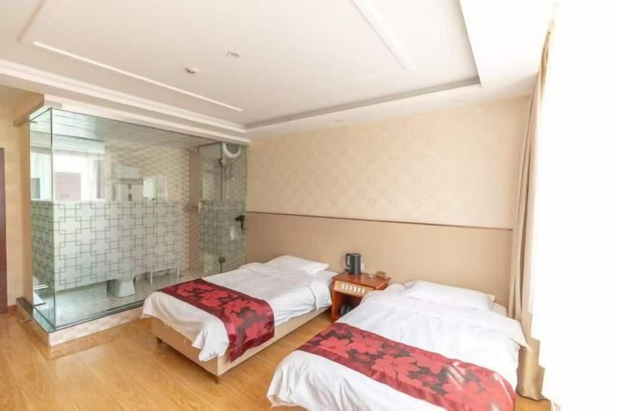 Ein Hotelzimmer mit zwei Betten, einer Duschkabine und einem verglasten Badezimmer.