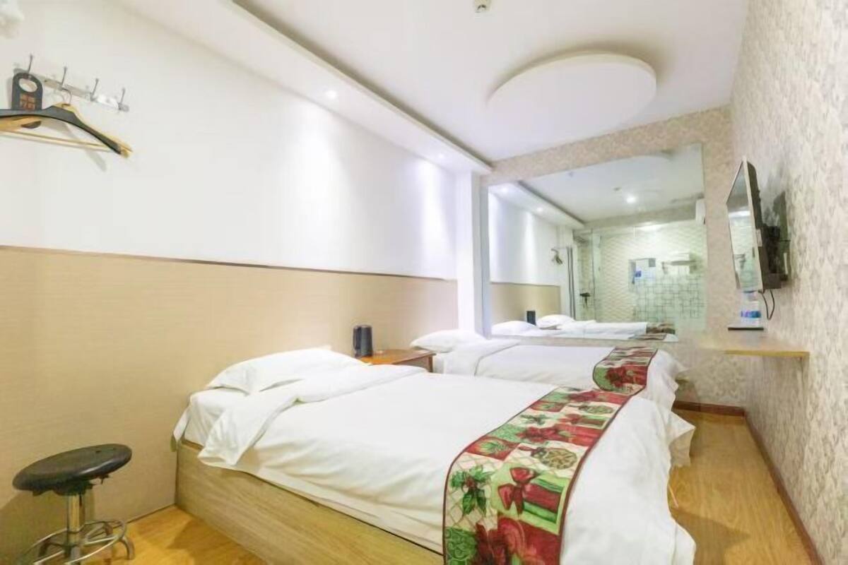 Ein Hotelzimmer mit zwei Betten, einem kleinen Hocker, einem Spiegel und einem Fernseher an der Wand.