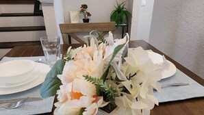 Een eettafel gedekt met witte borden, bestek en een bloemstuk van witte bloemen in een gestructureerde doos.