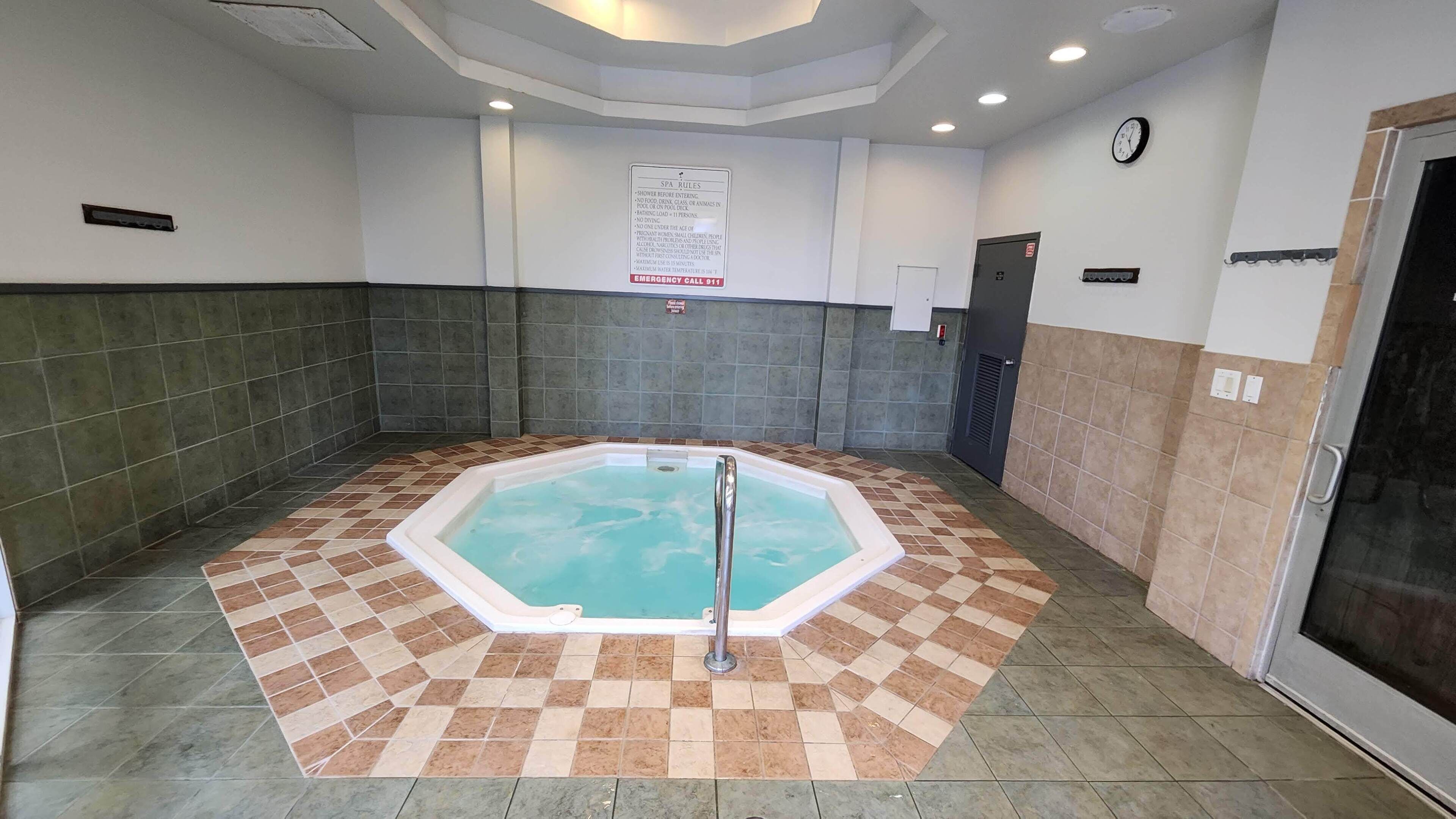 Un espace spa comprenant un jacuzzi, des murs carrelés et un panneau indiquant les règles à respecter dans le spa.