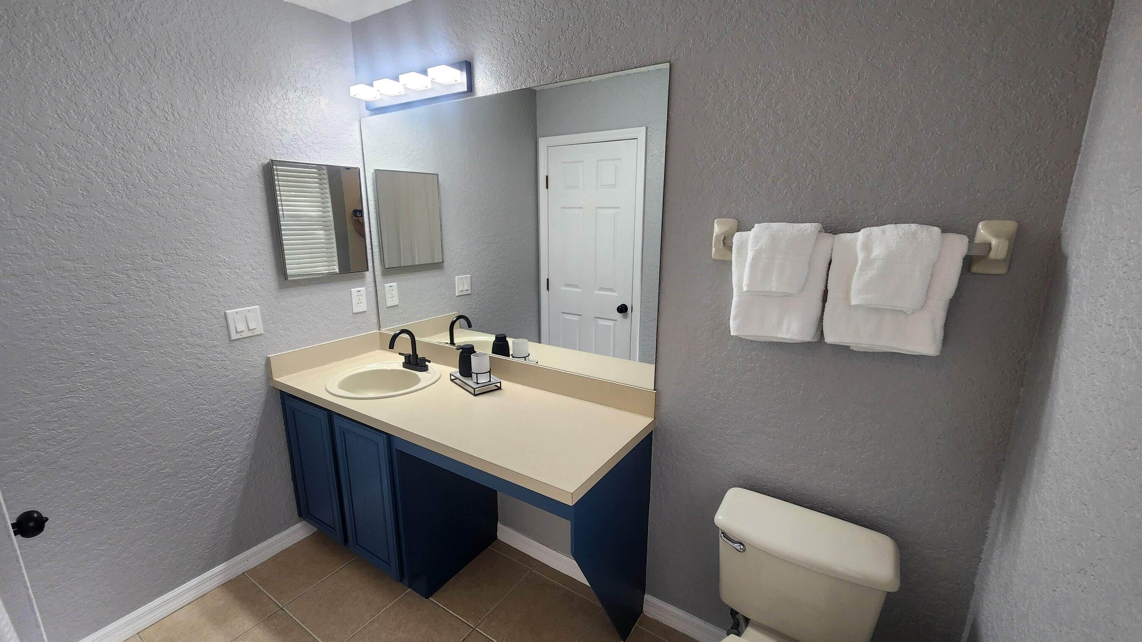 Een badkamer met een dubbele wastafel, een spiegel, een toilet en twee handdoeken aan een handdoekrek.