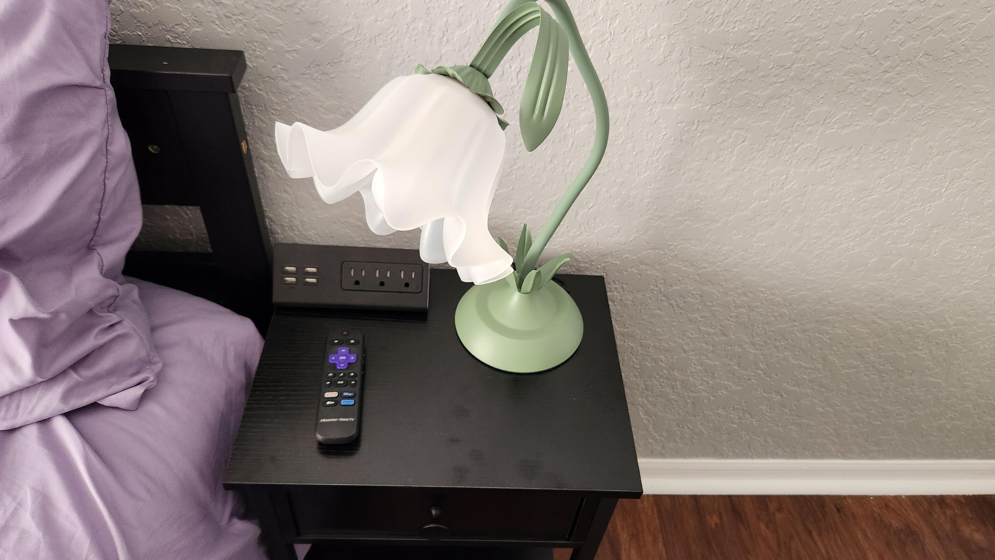 A bedside table with a remote control, a green lamp, and a purple blanket.
