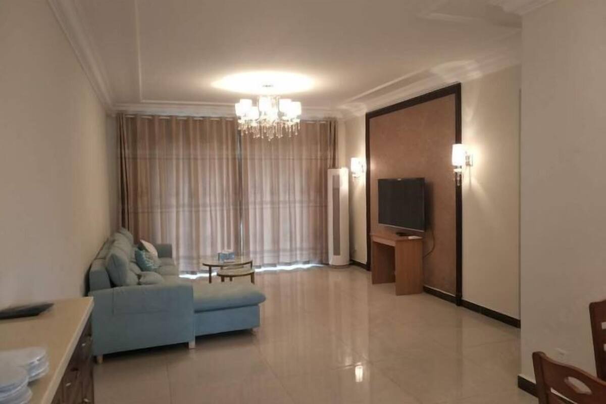 Una sala de estar con un sofá, un televisor, una araña, cortinas y un televisor de pantalla plana sobre un mueble.