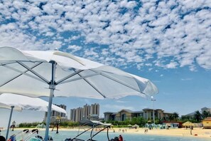 A beach scene with umbrellas, a boat, and buildings in the background. - Qidong Risheng Donghai Holiday Apartment (Qidong)
