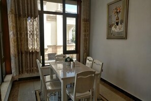 A dining area with a table and chairs, a window with curtains, and a framed picture on the wall. - Qidong Risheng Donghai Holiday Apartment (Qidong)