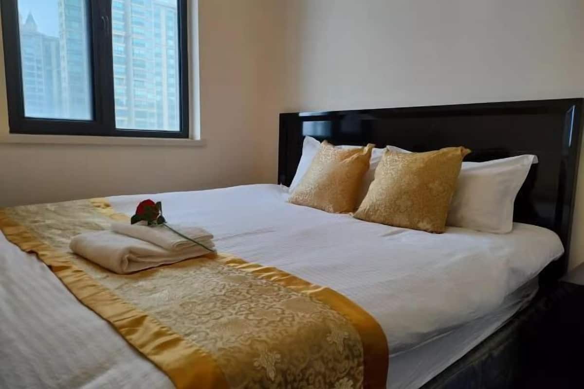 Una cama bien hecha con un edredón estampado, dos almohadas y una toalla doblada con un motivo de rosa.