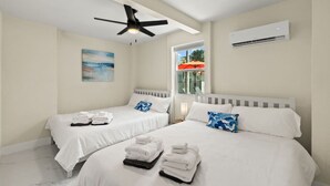 A hotel room with two beds, a ceiling fan, an air conditioning unit, and a window with a view of the outside. - Steps to BEACH/POOL/Downtown (Fort Myers Beach)