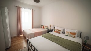 A bedroom with two beds, a wooden floor, a white door, and a window with curtains.