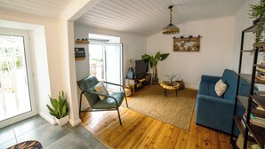 A living room with a wooden floor, a blue sofa, a green chair, a TV, and a bookshelf.