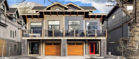 A modern two-story house with a balcony, garage doors, and a red door.
