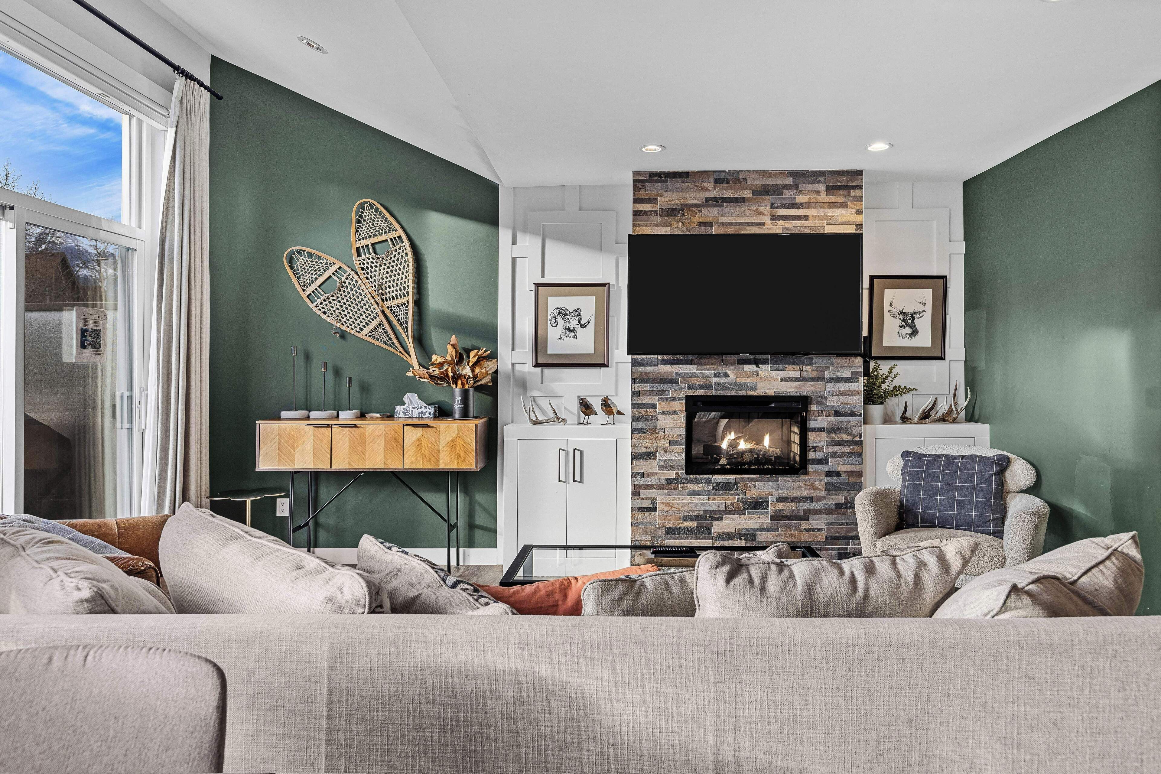 Una sala de estar moderna con chimenea, paredes verdes y un ventanal grande.