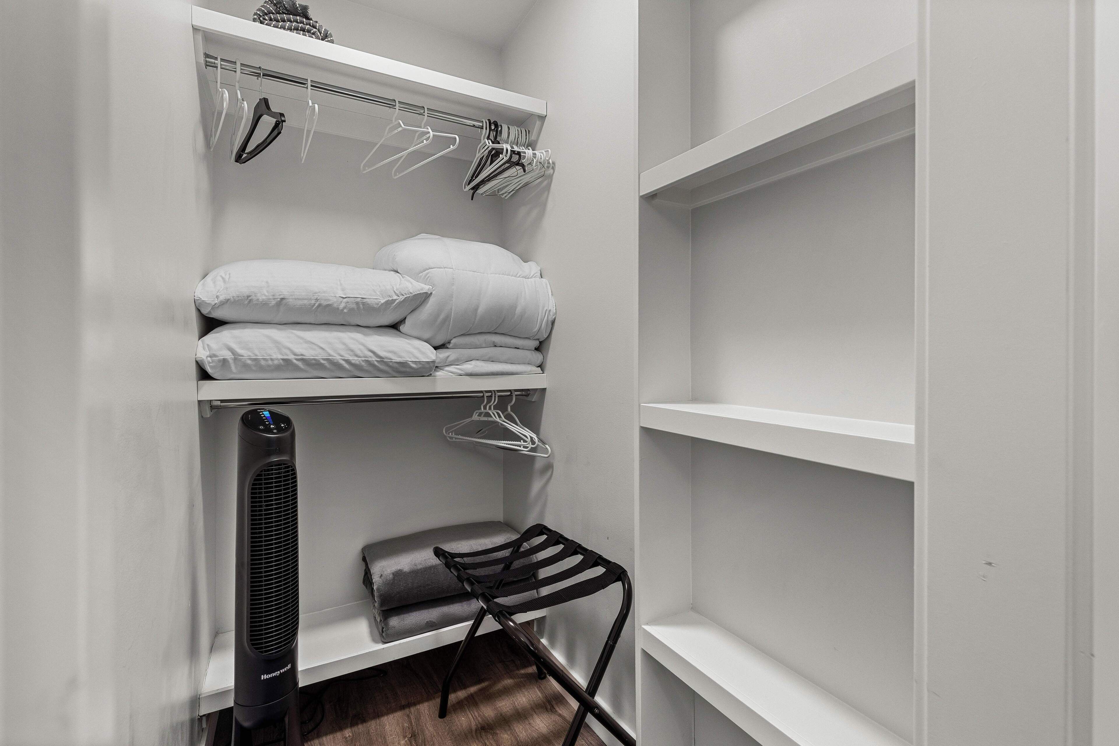 Un armario blanco con estantes, una barra para colgar ropa y una silla negra.