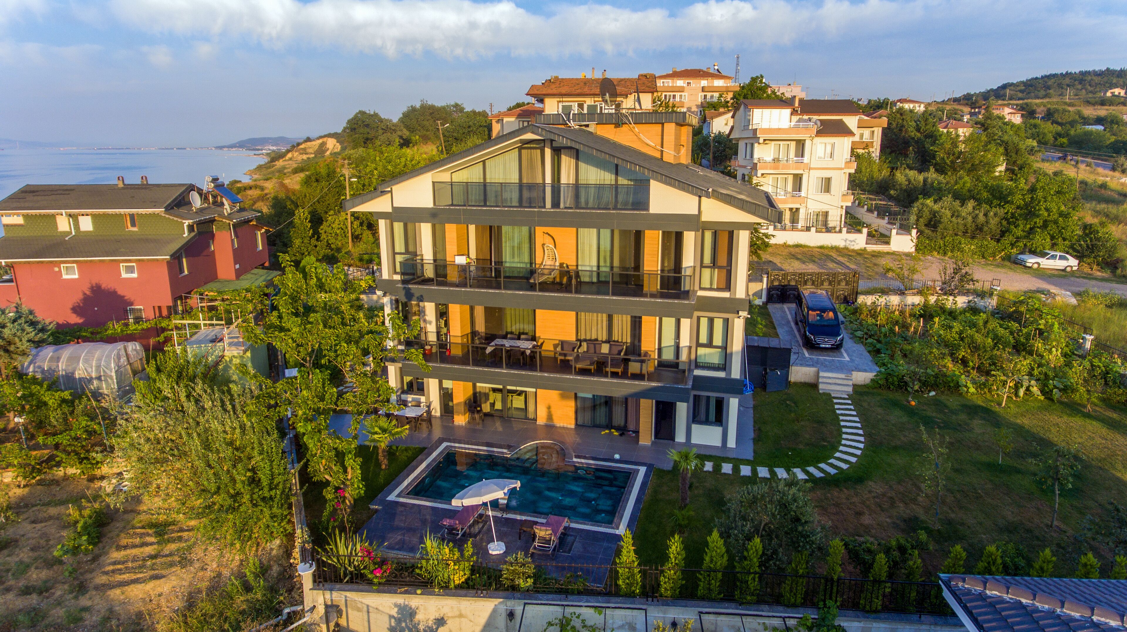 A modern two-story house with a large balcony, a swimming pool, and a view of the sea.