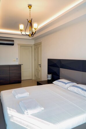 A hotel room with a large bed, a bedside table, a dresser, a chandelier, and a door. - Luxury cihan villa  (Termal)
