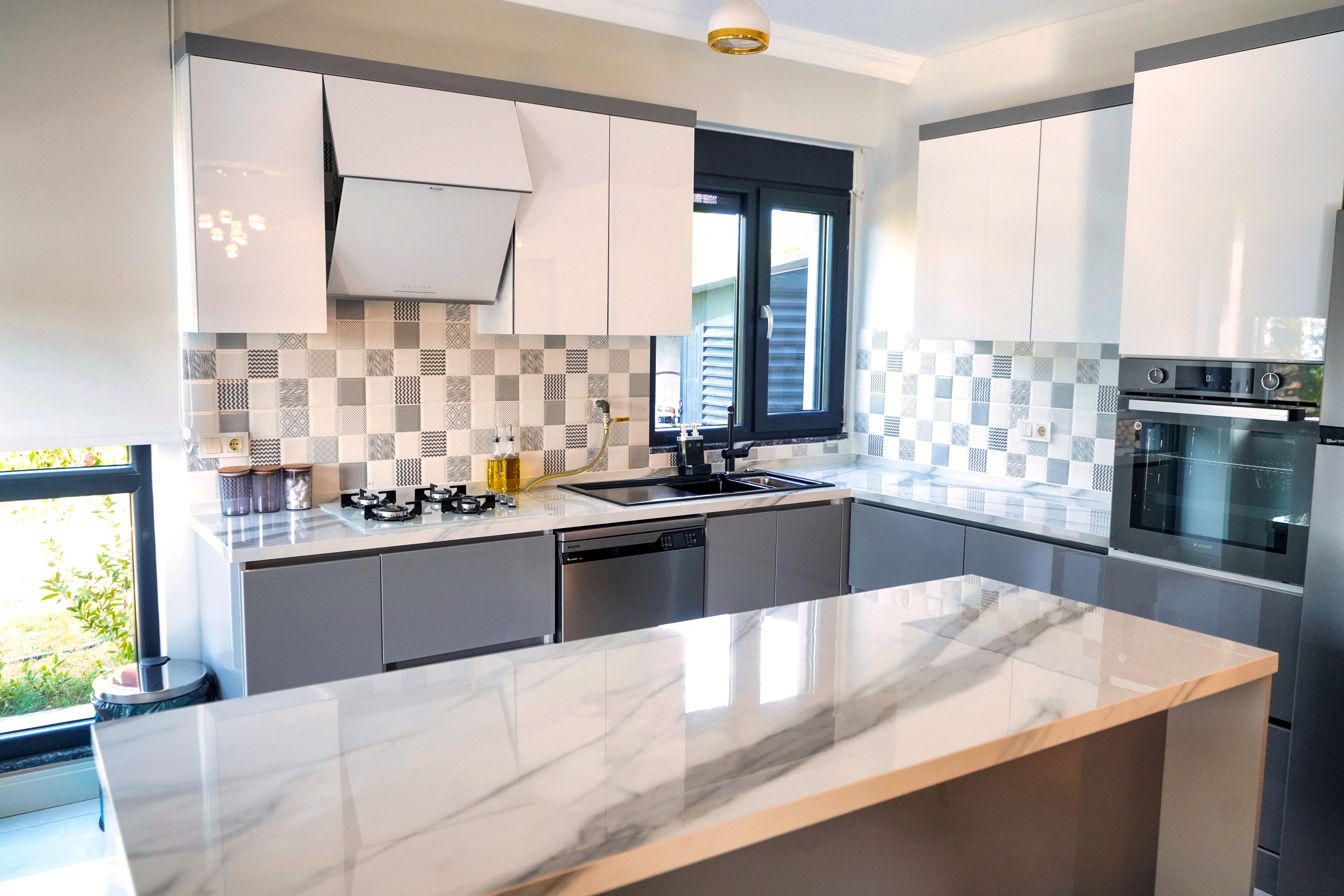 A modern kitchen with grey cabinets, a marble countertop, a built-in oven, and a window with blinds.