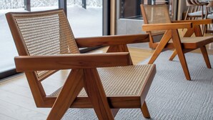 A modern interior with wooden lounge chairs and tables, large windows with a view of snow-covered trees. - Mori Casa (Kutchan)