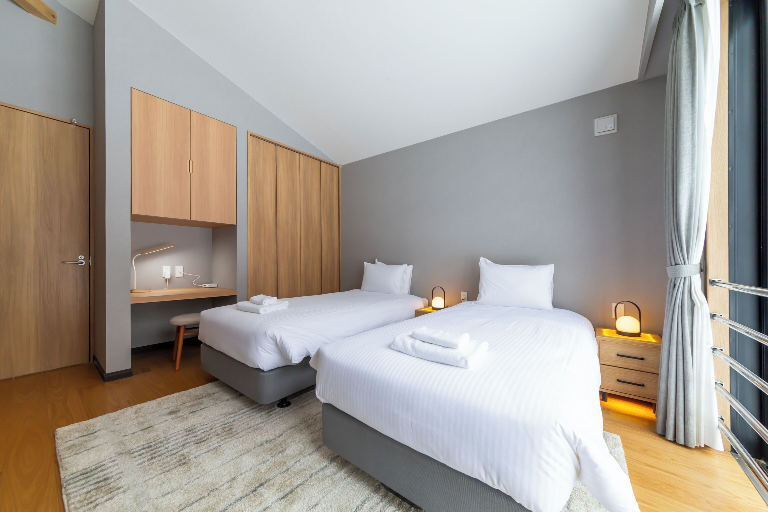 A bedroom with two beds, a desk, and a wardrobe.