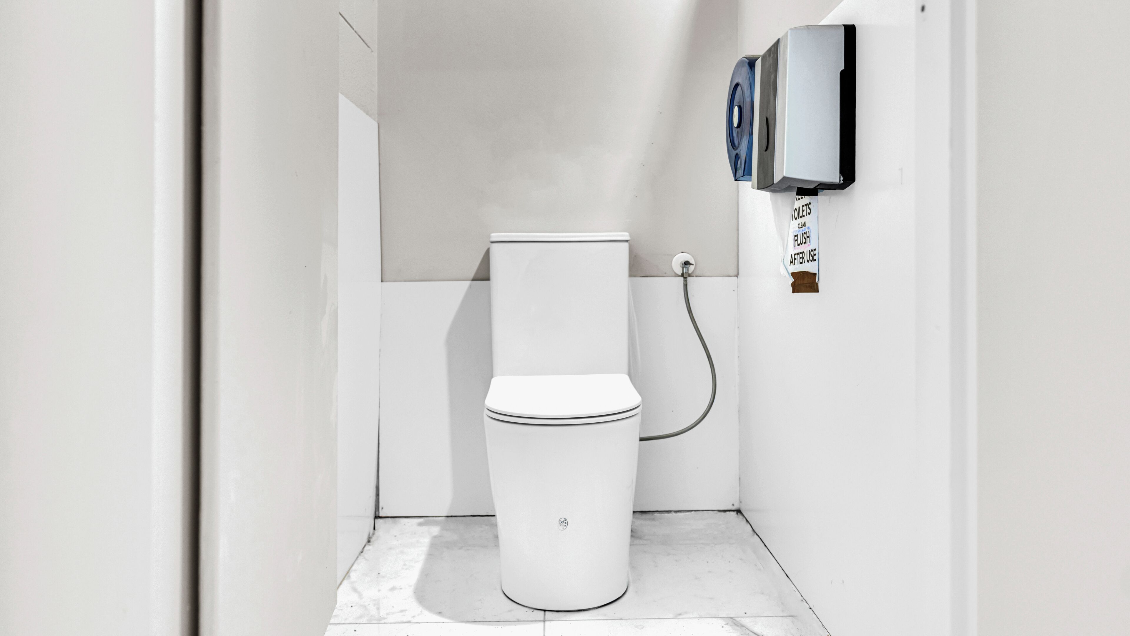 Casa de banho moderna e compacta com sanita branca, sistema de descarga embutido na parede e cano visível.