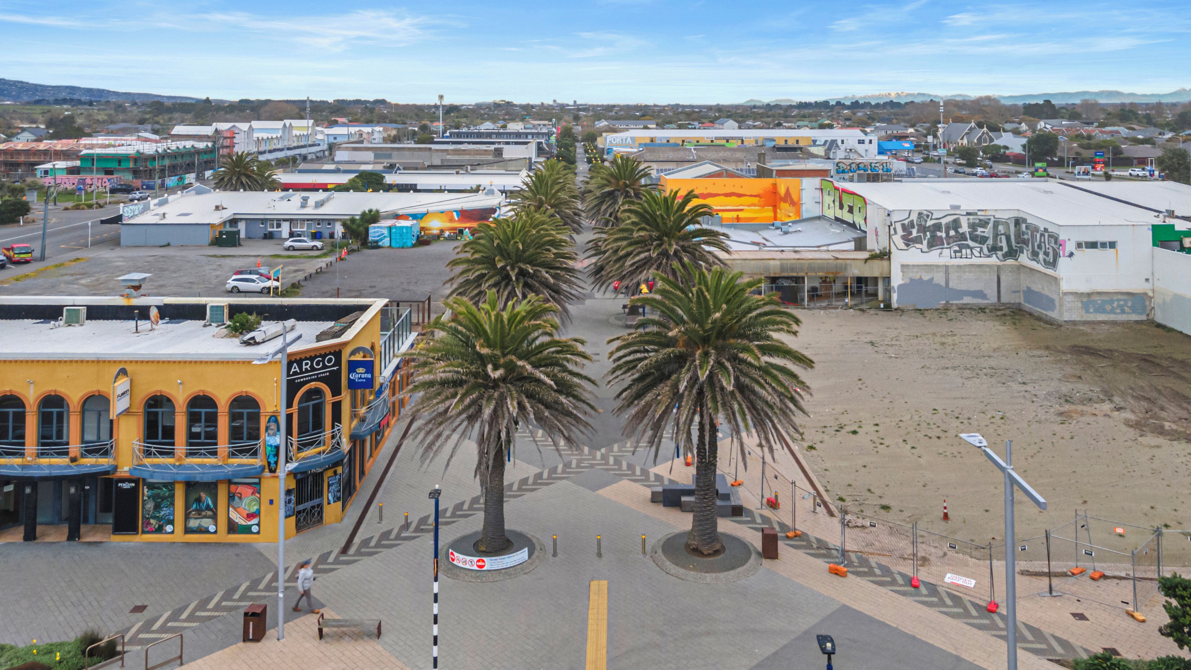 Vista de la calle con un edificio amarillo identificado como 'ARGO' y palmeras a lo largo de la carretera.