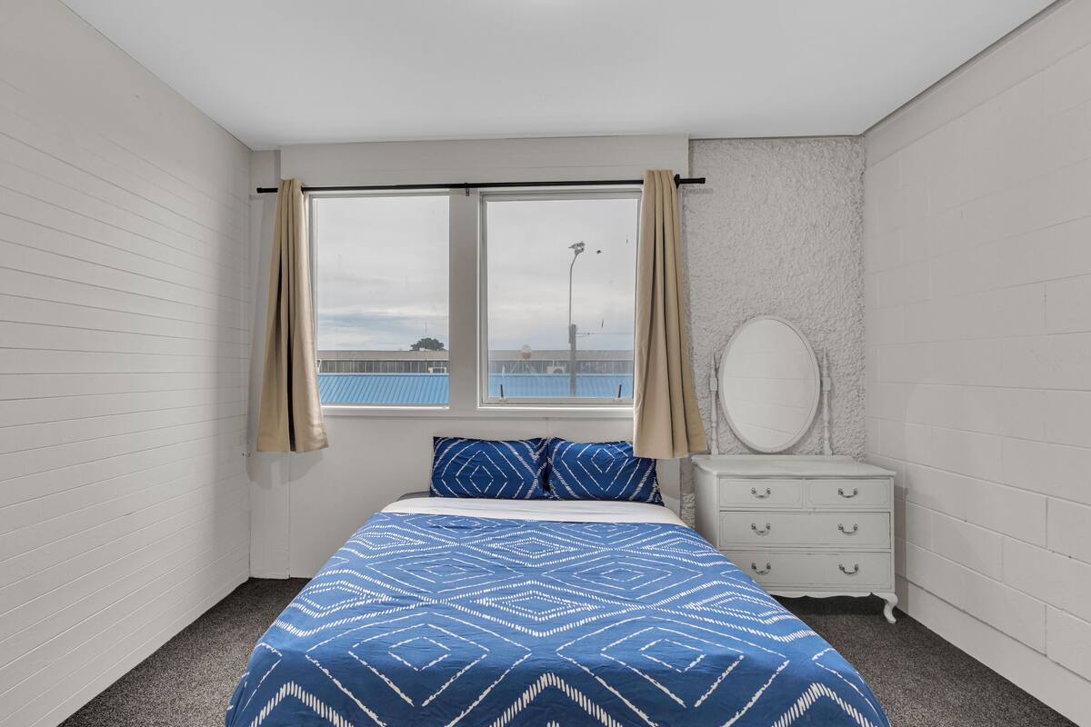 Een slaapkamer met een bed, een dressoir, een spiegel en een raam met gordijnen.