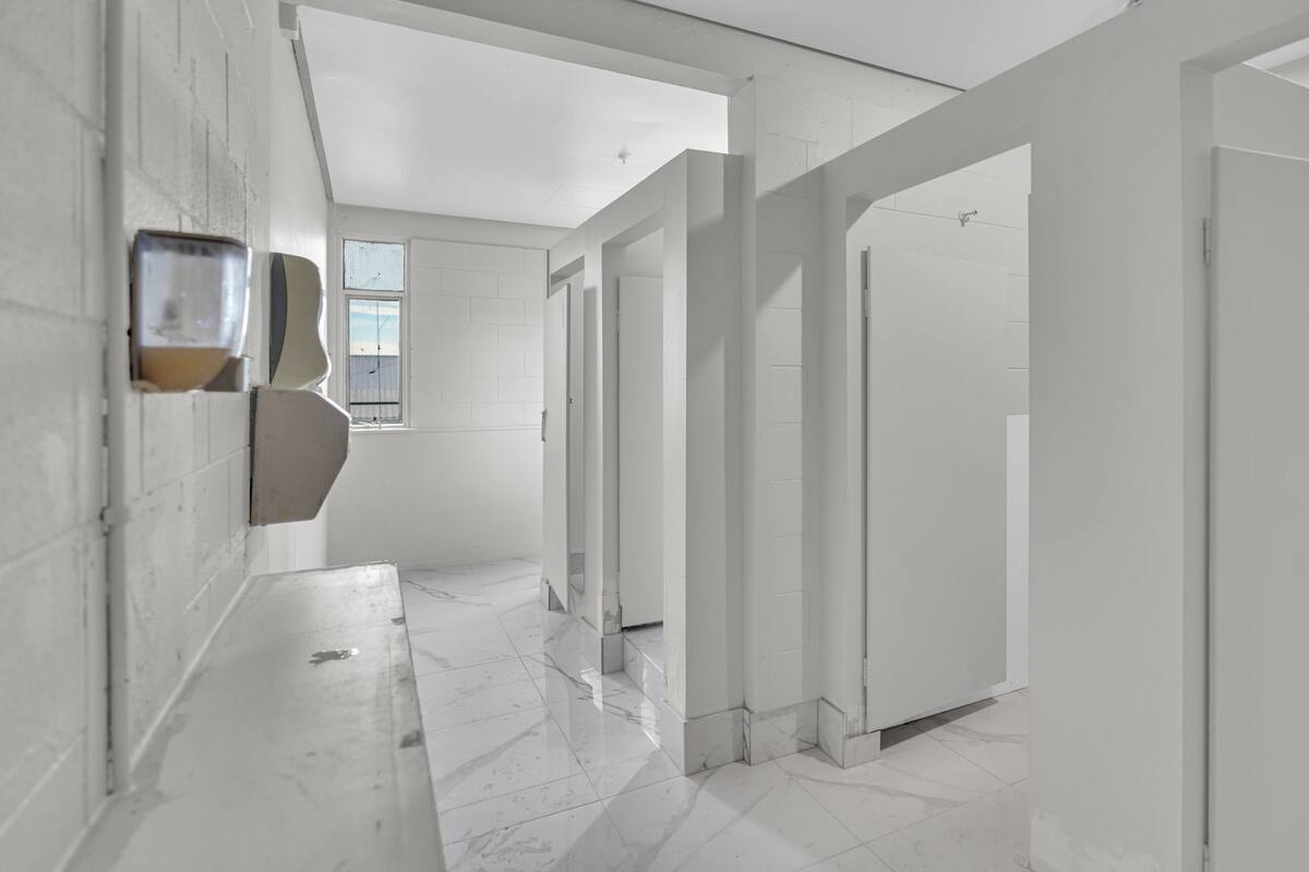 Een moderne, witte gang met een marmeren vloer, die leidt naar een badkamer met toilet en douche.