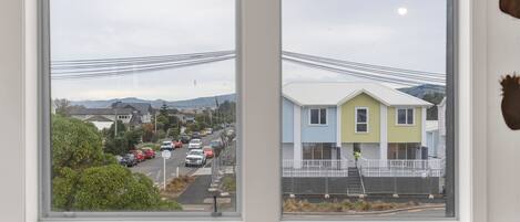 Vista a través de una ventana que muestra una calle con casas, una carretera y líneas eléctricas.