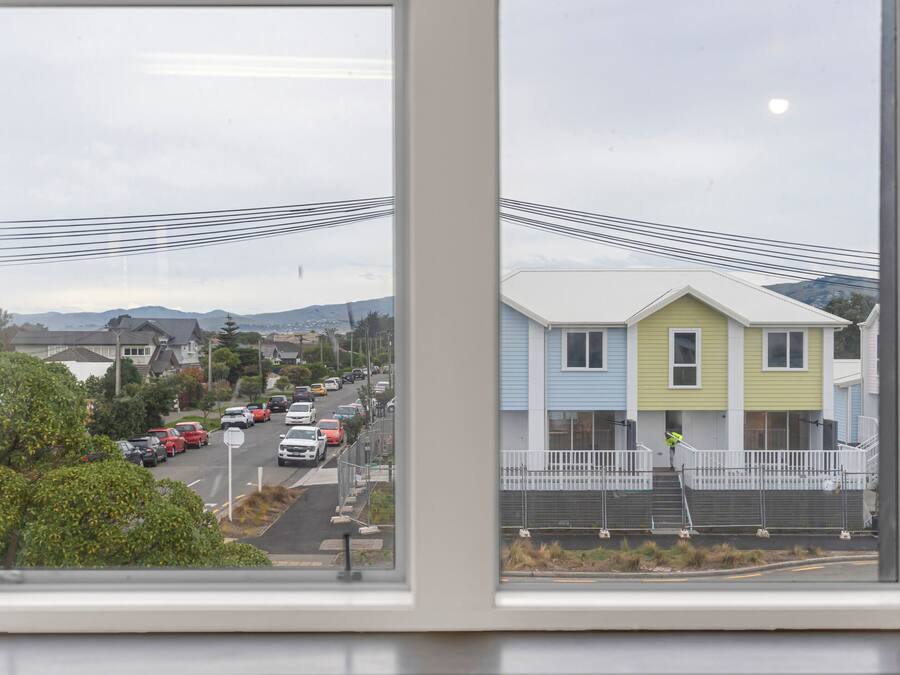 A view through a window of a street with houses, a road, and power lines.