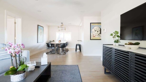 Un salon moderne comprenant un coin repas, un meuble de rangement noir pour les appareils électroniques et un grand téléviseur.