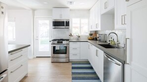 Une cuisine moderne avec des meubles blancs, des appareils en acier inoxydable et un tapis à motifs bleus.