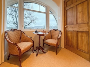 A room with two ornate chairs, a small round table with chess pieces, and a large wooden door.