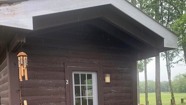 A small wooden cabin with a porch, a fishing rod, and a grill. - Strawberry Crossroads (Pittsville)