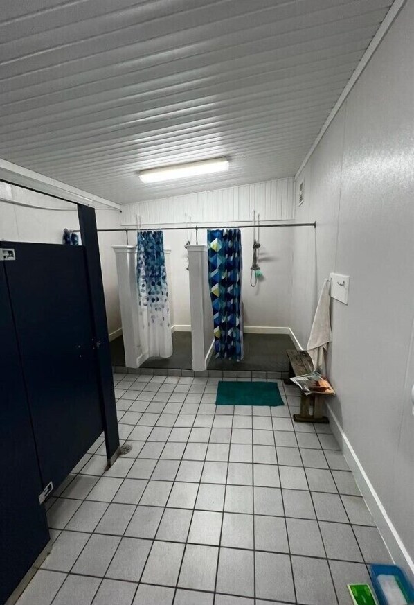 Un baño con suelo de baldosas, zona de ducha con cortinas estampadas y un perchero.