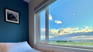 Une chambre avec une grande fenêtre, un lit soigneusement fait et un tableau encadré accroché au mur.