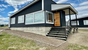 Une maison moderne à deux étages, avec une façade sombre, de grandes fenêtres et une porte d’entrée en bois.