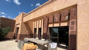 An outdoor patio area with a long table and chairs, a covered seating area, and a building entrance with glass doors. - Beautiful family villa near Marrakech, with large garden, private swimming pool (Centre Commune Ouled Hassoune)