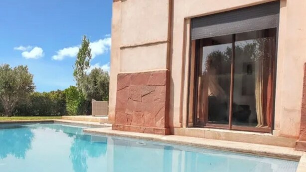 A swimming pool adjacent to a building with stone walls and a large sliding glass door. - Beautiful family villa near Marrakech, with large garden, private swimming pool (Centre Commune Ouled Hassoune)