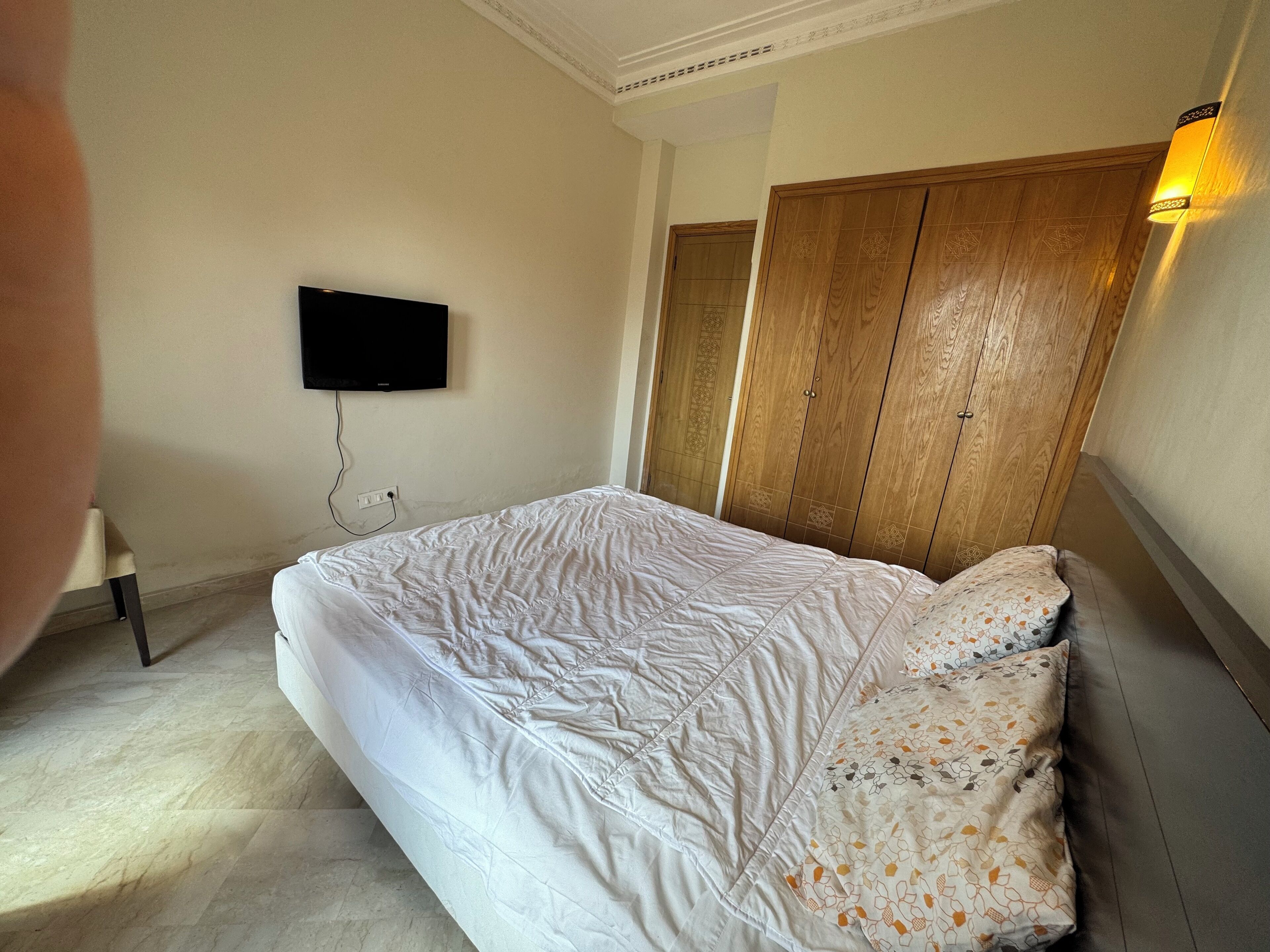 A bedroom with a bed, a television mounted on the wall, and a wardrobe.