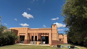 A building with a flat roof and a central tower, surrounded by a well-maintained lawn and a pool area. - Beautiful family villa near Marrakech, with large garden, private swimming pool (Centre Commune Ouled Hassoune)